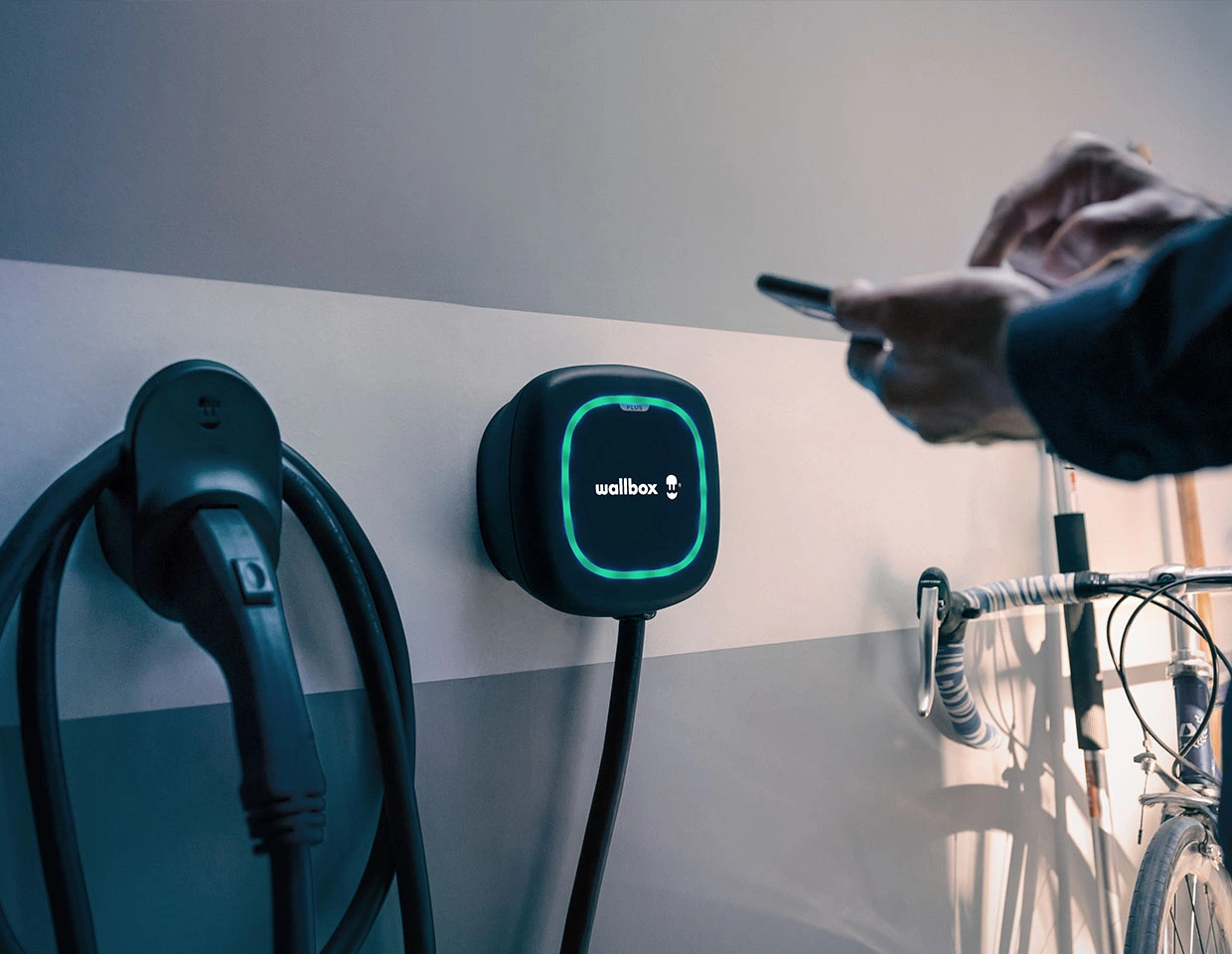 Otthoni falra szerelt elektromos autó töltő okos vezérléssel, töltőkábel és Wallbox alkalmazás használata közben.